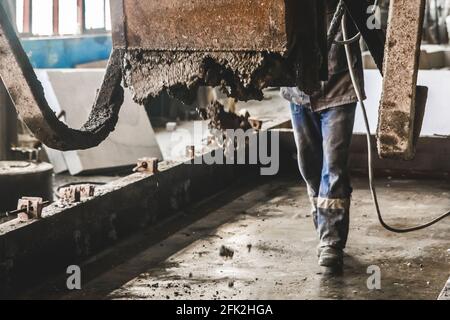 L'ouvrier industriel contrôle le flux du mélange de gravier de béton d'un mélangeur à l'atelier de renforcement, foyer sélectif. Banque D'Images