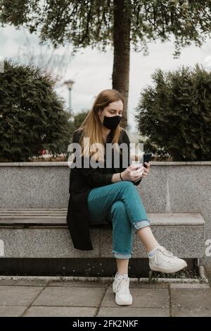 Femme avec masque facial utilisant un smartphone à l'extérieur dans la ville Banque D'Images