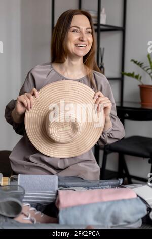 Femme riante posant avec chapeau de paille emballer bagages se préparer pour voyager méthode de konmari Banque D'Images