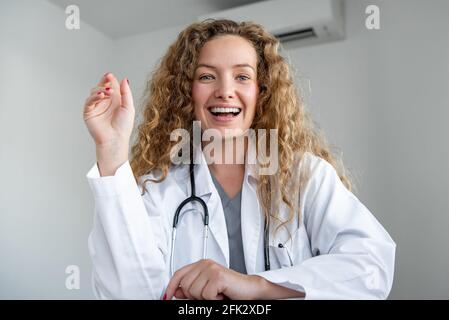 Gaie souriante jeune femme médecin regardant la caméra saluant patient en ligne via les appels vidéo, les concepts de service de conspulation médicale à domicile Banque D'Images