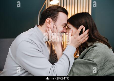 Couple d'âge moyen amoureux tenant le visage de l'autre, en touchant les têtes. Assis en face l'un de l'autre dans le confort de la maison. Se regardant les uns les autres et les s. Banque D'Images