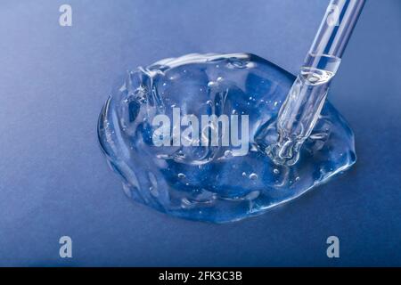 Gel échantillon de texture de sérum produit cosmétique pour la santé de la peau dans la pipette. Collagène en gel transparent avec compte-gouttes sur fond bleu. Échantillon de produit chimique Banque D'Images