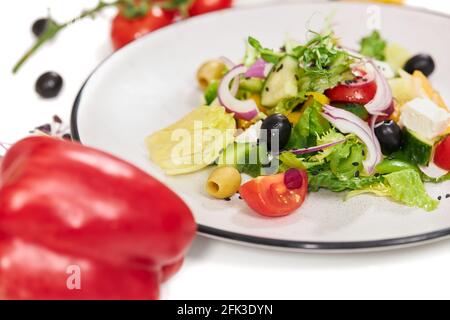 Gros plan de délicieuses salades de légumes avec des tomates appétissantes, des olives, des verts, des oignons et du fromage feta sur fond blanc. Concept de nutrition appropriée pour la perte de poids. Banque D'Images