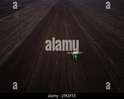 Vue aérienne d'un tracteur vert moderne ensemençant un champ agricole Banque D'Images