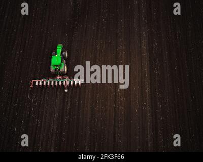 Vue aérienne d'un tracteur vert moderne ensemençant un champ agricole Banque D'Images