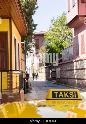 Panneau jaune de toit de cabine de taxi avec mot turc TAKSI. Il y avait un parking sur la petite vieille rue d'Antalya. Un couple peu concentré s'éloigne sur l'arrière-plan. Banque D'Images