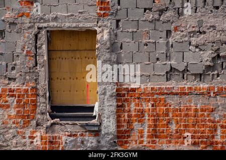 Bloc de ciment creux et mur de brique rouge d'un déchiré bâtiment en bas avec une porte couverte de lambris Banque D'Images