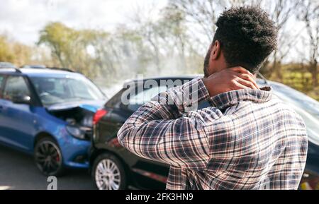 Jeune homme frottant le cou dans la douleur de blessure de coup debout par une voiture endommagée après un accident de la route Banque D'Images