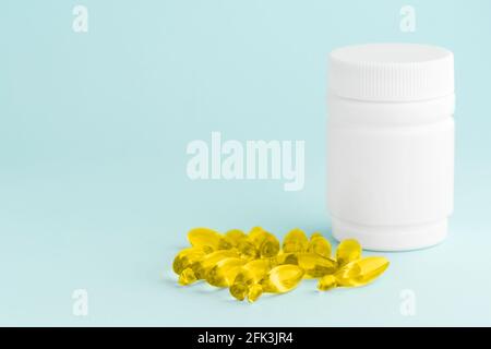Capsules de supplément jaune d'huile de poisson omega-3 isolé et flacon en plastique blanc sur la surface bleue. Concept de soins de santé Banque D'Images