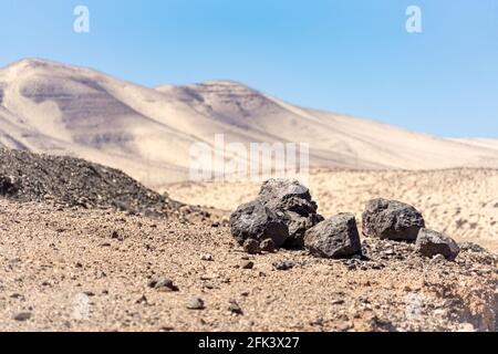 Collines blanches parsemées de roches de lave noires dans un désert paysage sous un ciel bleu sans nuages Banque D'Images