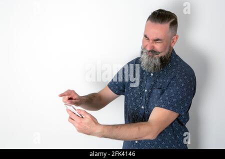 taille basse avec une grande barbe à demi grise, utilisant son smartphone avec un visage dégoûté. Caucasien 40-45 ans Banque D'Images