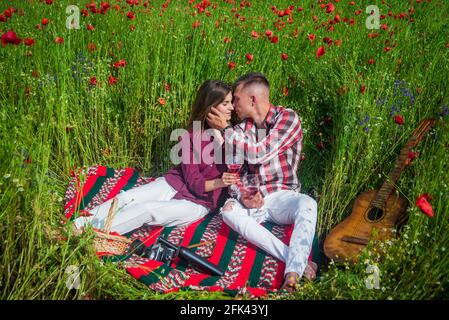 les amateurs de guitare boivent du vin dans le champ de fleurs. musique. couple amoureux. homme et femme dans le champ de pavot. Banque D'Images