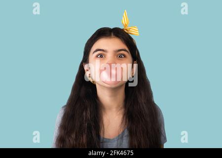 Adorable jeune fille indienne soufflant de la bulle de la gomme à mâcher, ayant l'expression du visage excitée sur fond bleu Banque D'Images