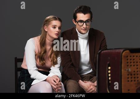 un couple concentré en vêtements rétro regardant la télévision isolée sur le noir Banque D'Images