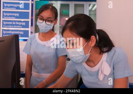 Deux femmes cambodgiennes assistantes dentaires / réceptionnistes, travailleurs de première ligne, tous deux portant un masque facial / revêtement, tout en vérifiant un ordinateur dans une clinique dentaire pendant la pandémie du coronavirus. Phnom Penh, Cambodge, Indochine. 22 janvier 2021. © Kraig Lieb Banque D'Images