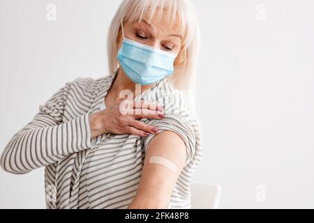 Femme âgée montrant bras vacciné après injection d'antiviral, White Studio Banque D'Images