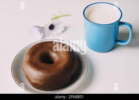 Délicieux beignet de chocolat frais sur fond blanc. Appétissant beignet glacé savoureux prêt à manger avec une tasse de lait frais Banque D'Images