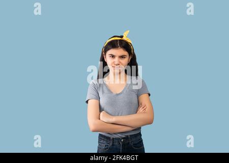 Émotions des gens. Portrait d'une adolescente indienne offensé posant avec des bras pliés, regardant l'appareil photo sur fond bleu Banque D'Images