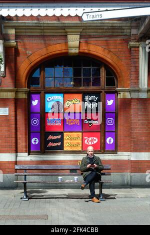 Un homme d'âge moyen assis sur un banc à l'extérieur d'une fenêtre de magasin de détail du Royaume des Sweets dans le centre commercial de Windsor Station , Berkshire Angleterre Royaume-Uni Banque D'Images