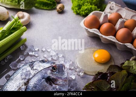 Cadre d'ingrédients de cuisson crus pour des aliments savoureux et sains. dorado frais poisson sur glace, légumes, oeufs sur fond de béton gris vue de dessus. Banque D'Images