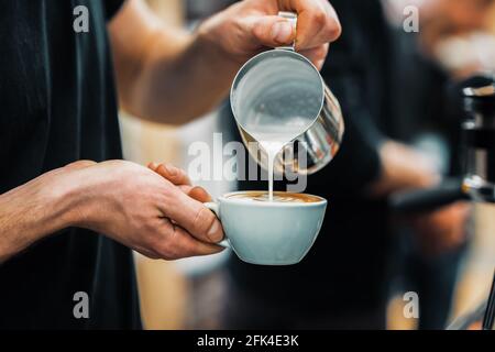 Le barista verse du lait chaud dans une tasse à café pour préparer des latte. Culture du café et préparation professionnelle du café, service et restauration Banque D'Images