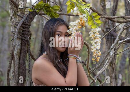 Gros plan d'une jeune femme aux longs cheveux bruns dans un cadre boisé, avec des fleurs accrochées d'une vigne Banque D'Images