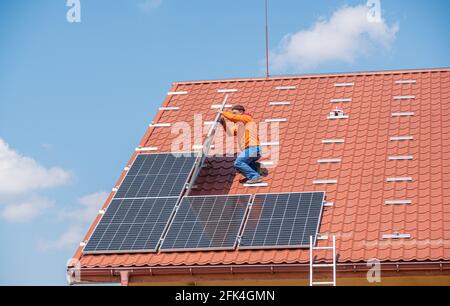 Un travailleur installe des panneaux solaires d'une centrale électrique sur le toit d'une maison privée. Banque D'Images