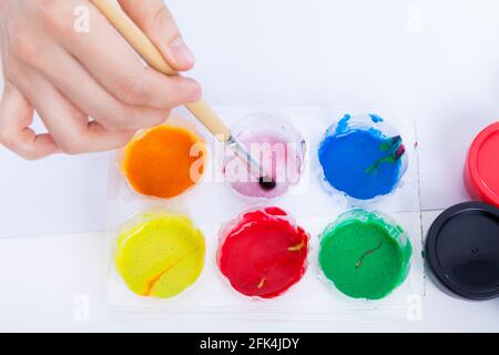 Gros plan, main humaine plongeant le pinceau dans de l'aquarelle sur la palette. Palette de faible profondeur de champ (DOF) mise au point. Prise de vue en studio Banque D'Images