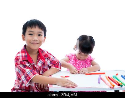 Petits enfants asiatiques jouant et créant des jouets à partir de la pâte de jeu sur la table. Garçon souriant et regardant l'appareil photo, sur fond blanc. Renforcer l'image Banque D'Images