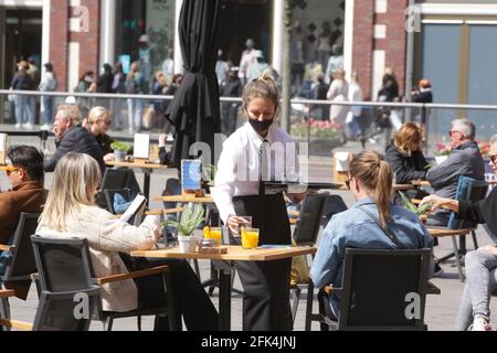 Amsterdam, pays-Bas. 28 avril 2021. Une serveuse portant un masque facial de protection dessert les clients sur la terrasse d'un restaurant du Beursplein, dans le centre d'Amsterdam, dans le cadre de la pandémie du coronavirus, le 28 avril 2021 à Amsterdam, aux pays-Bas. Le gouvernement néerlandais prend aujourd'hui un pas important pour relâcher le blocage du coronavirus, après six mois de fermeture des terrasses et des magasins rouvrent mais ferment à 6 h à travers le pays. (Photo de Paulo Amorim/Sipa USA) Credit: SIPA USA/Alay Live News Banque D'Images