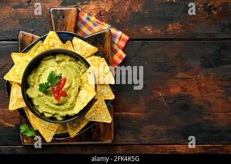 Guacamole. Sauce mexicaine traditionnelle latinaméricaine dans un bol noir avec avocat et ingrédients et nachos de maïs. Propagation de l'avocat. Vue de dessus. Copyspa Banque D'Images