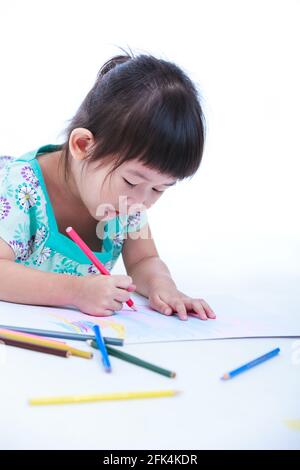 Une jolie fille asiatique se trouve sur le sol et dessine sur du papier. Les concepts de créativité et d'éducation renforcent l'imagination de l'enfant. Prise de vue en studio. Sur wh Banque D'Images