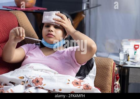 Une femme indienne de taille moyenne portant un masque nasal chirurgical, un front froid et la vérification de la température corporelle avec un thermomètre, concept de soins de santé Banque D'Images