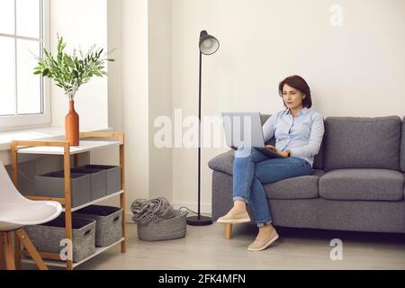 Femme de direction décontractée travaillant sur un ordinateur portable assis sur un canapé confortable dans un bureau moderne et lumineux. Banque D'Images