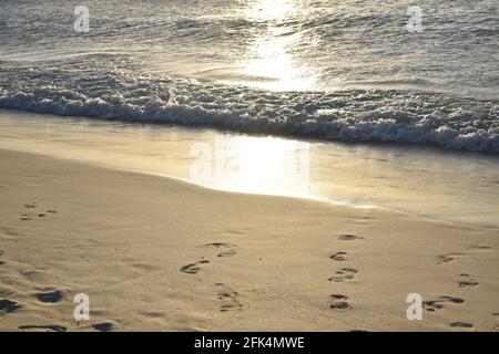 plage avec empreintes de pas et vagues en arrière-plan avec coucher de soleil réflexion dans de l'océan Banque D'Images