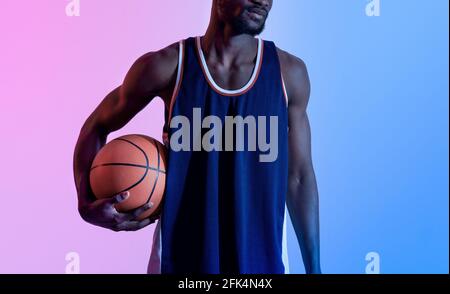Gros plan d'un joueur de basket-ball noir tenant le ballon dans un éclairage au néon Banque D'Images