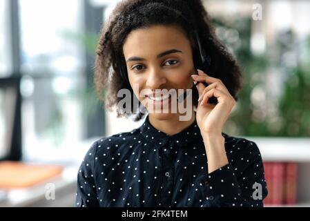 Portrait en gros plan d'une charmante jeune femme à poil dur, charmante et mixte, dans un casque, une chemise élégante, un employé de centre d'appels ou un opérateur de soutien, regardant directement l'appareil photo, souriant amical Banque D'Images