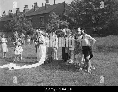 Dans les années 1950, historique, sur un terrain au bout de la terrasse des maisons victoriennes, un groupe d'hommes locaux - « The Heavy Gang » vêtu de vêtements pour femmes et de vêtements fantaisie debout pour une photo avant un spectacle pour le festival « Day », Angleterre, Royaume-Uni. Les acteurs amateurs ici sont en costumes différents, y compris Guinevere, la légendaire reine du roi Arthur. May Day était une tradition ancienne qui célébrait l'arrivée du printemps et de l'été et les artistes s'habillent et redonnent de vieux folklore et des histoires en dansant autour d'un grand poteau en bois, un maypole, une activité populaire. Banque D'Images