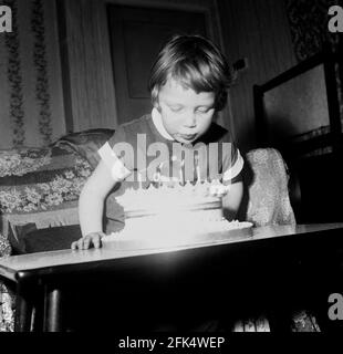 années 1960, historique, à l'intérieur d'une pièce, sur une petite table basse, une petite fille soufflant sur les quatre bougies allumées sur son gâteau d'anniversaire. Banque D'Images