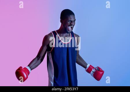 Sportif noir agressif en gants de boxe criant en colère dans la lumière du néon. Concept de sports de combat Banque D'Images