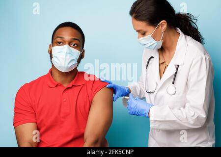 Médecin injectant l'homme noir donnant le vaccin contre Covid-19, fond bleu Banque D'Images
