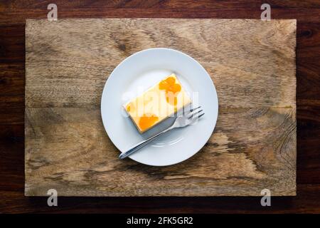 Un morceau de cheesecake avec des tranches de mandarine sur une assiette avec fourche sur fond en bois foncé Banque D'Images