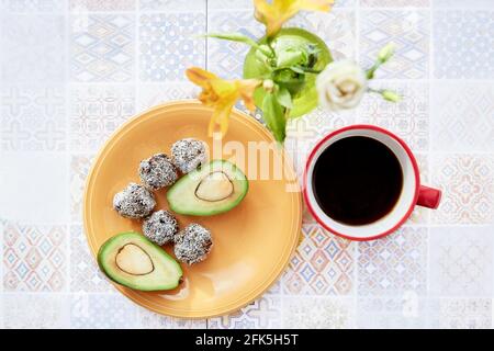 Petit déjeuner sain. Bonbons faits main en copeaux de noix de coco sur une assiette d'orange et une tasse de café sur carreaux de céramique. Vue de dessus Banque D'Images