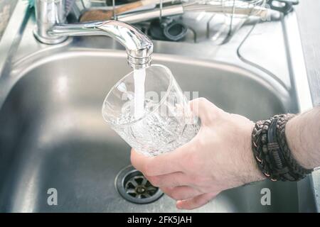Homme tenant UN verre au-dessus de l'évier de cuisine le remplir Avec l'eau qui coule du robinet Banque D'Images