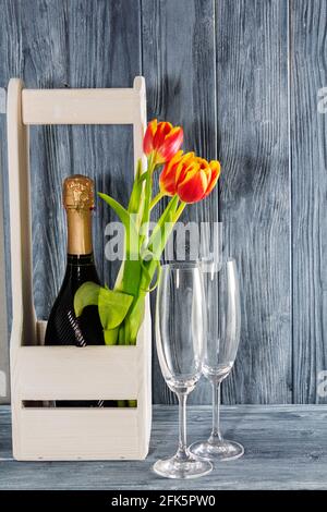 Une bouteille de champagne dans une boîte en bois. À côté de 2 verres de champagne et de fleurs de tulipes. Les vacances sont le 8 mars, fête des mères. Cadre romantique Banque D'Images