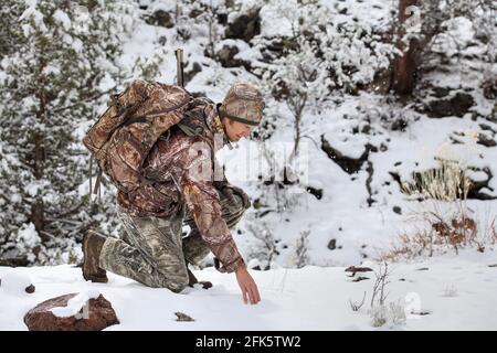 chasseur d'armes dans la scène neigeuse s'agenouillant pour inspecter les pistes de cerfs Banque D'Images