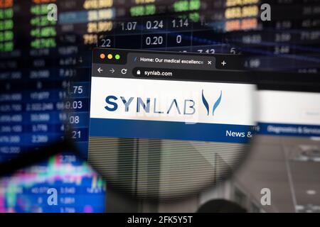 Logo de la société Synlab sur un site Web présentant des développements flous sur le marché boursier en arrière-plan, vu sur un écran d'ordinateur à travers une loupe Banque D'Images