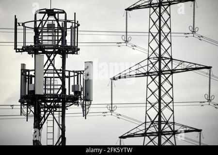 Gros plan d'un mât de téléphone de réseau cellulaire silhouetté et pylône électrique en treillis Banque D'Images