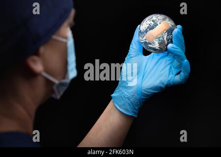 Infirmière ou médecin portant un masque facial et des gants chirurgicaux tenant la planète Terre bandée. Banque D'Images