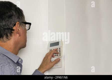 Homme avec des lunettes sur un clavier d'alarme sur un blanc mur Banque D'Images